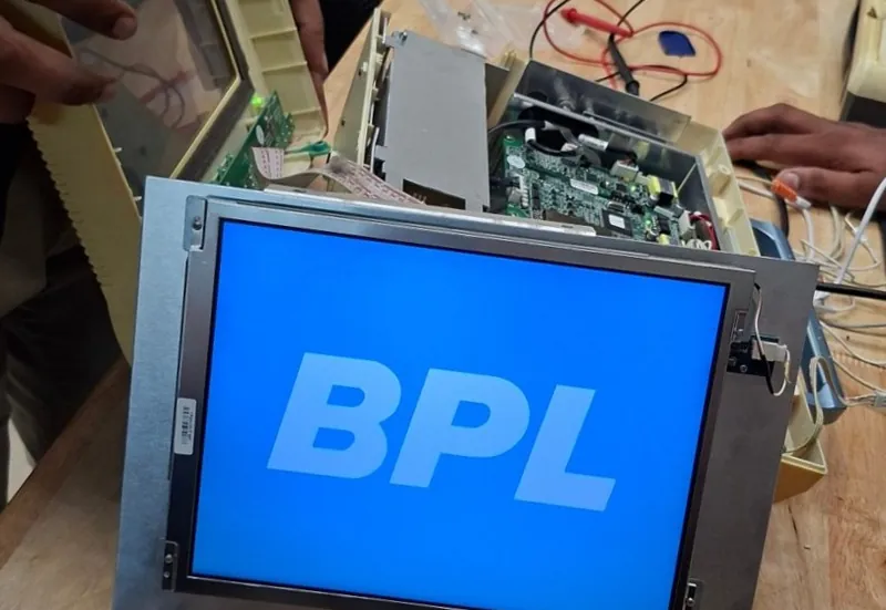 The patient monitor's bare screen showing only a blue BPL logo, with its opened case and circuit boards behind it