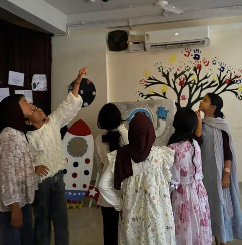 A group of girls looking up and pointing at the exhibition, with a painted rocket and an astronaut panel in front of them