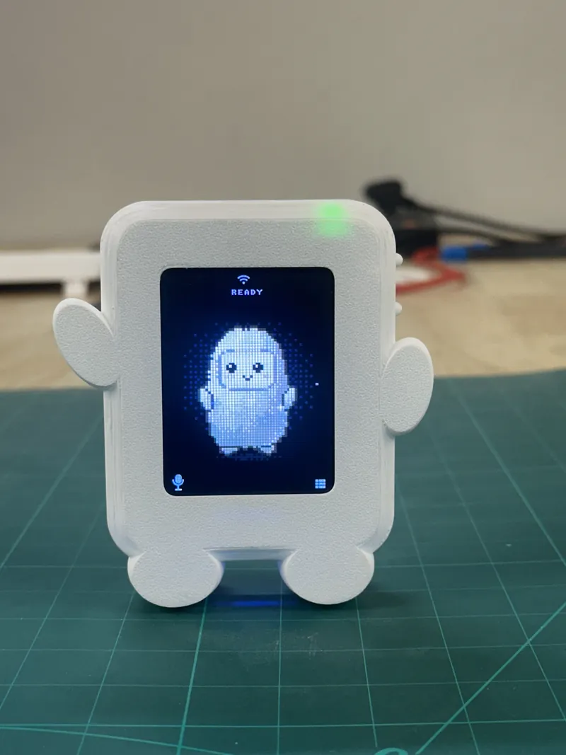 The UNIHIKER K10 in a white 3D-printed case with little arms and feet, its screen showing a pixel character and the word READY