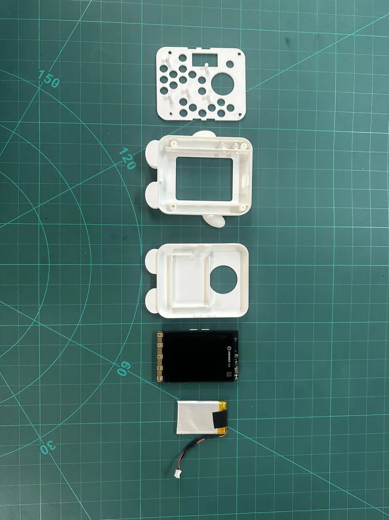 The parts laid out on a cutting mat: a 3D-printed front plate, two case halves, the UNIHIKER K10 board and a small battery