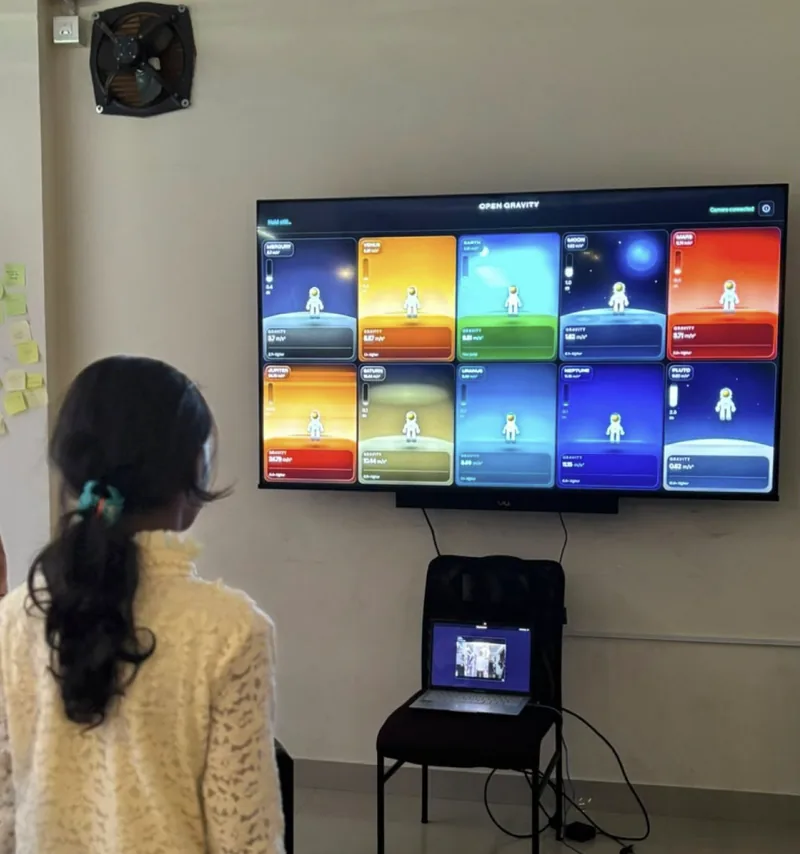 A student standing in front of a wall screen running Open Gravity, showing an astronaut on each planet
